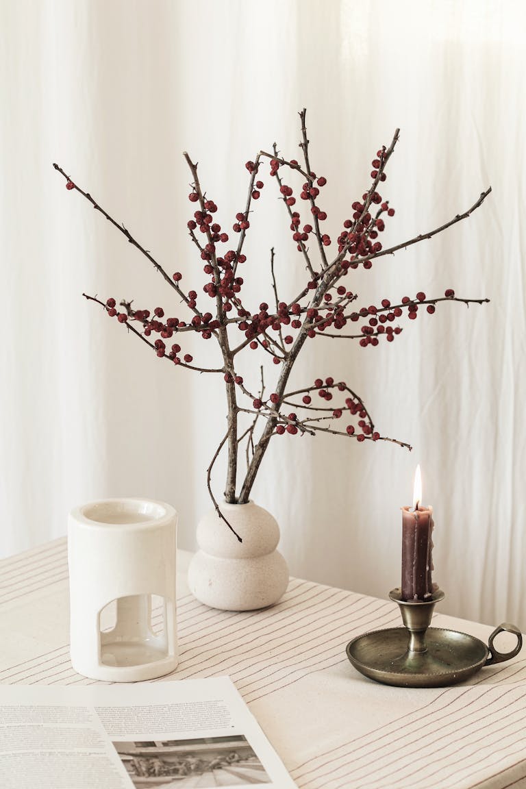 A minimalist interior setup featuring a burning candle, bare branches in a vase, and a cozy atmosphere.