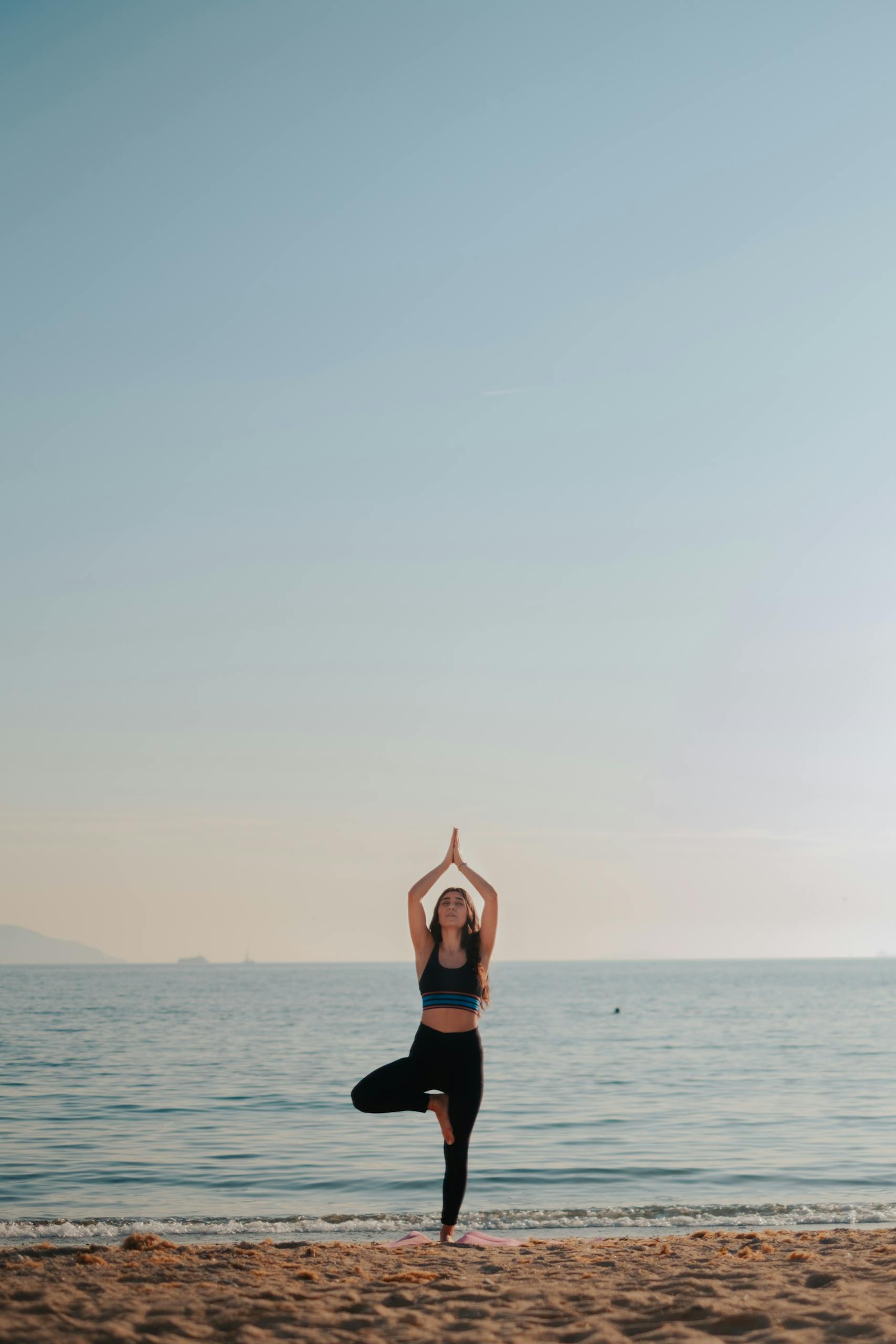 A woman performs a yoga pose on a tranquil beach, showcasing fitness and meditation at sunrise.