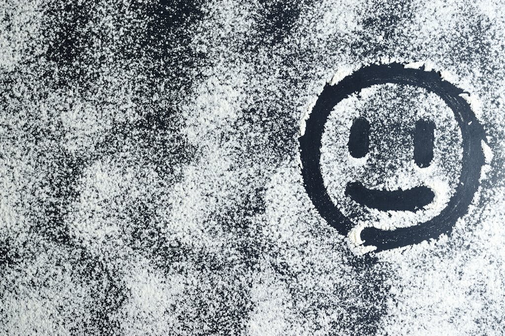 Artistic smiley face drawn through white powder on a black surface, creating an abstract texture.