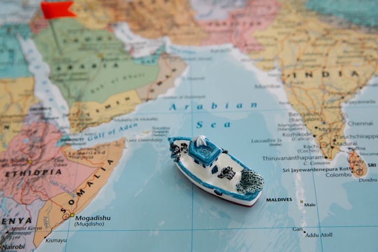 Close-up of a toy boat placed on the Arabian Sea section of a world map depicting regions around India.