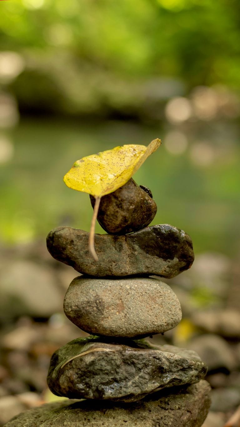 Balanced stones stacked outdoors with a yellow leaf, symbolizing tranquility and focus.